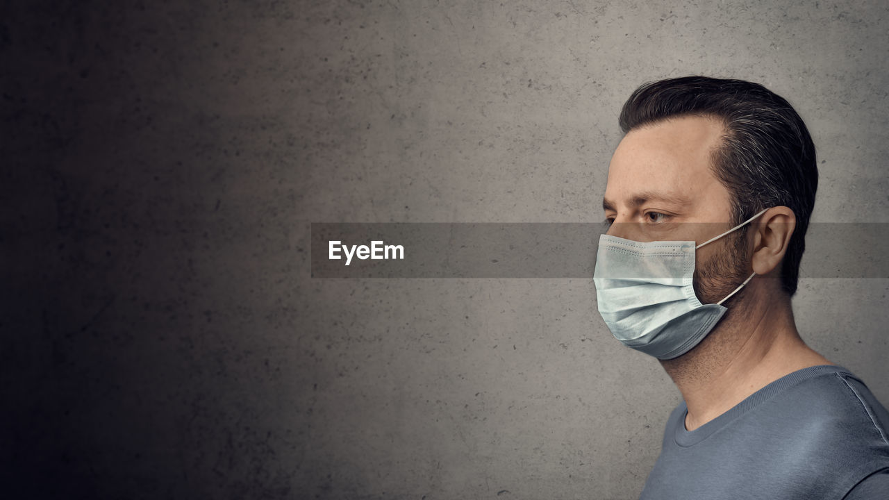 Man wearing surgical mask by gray wall