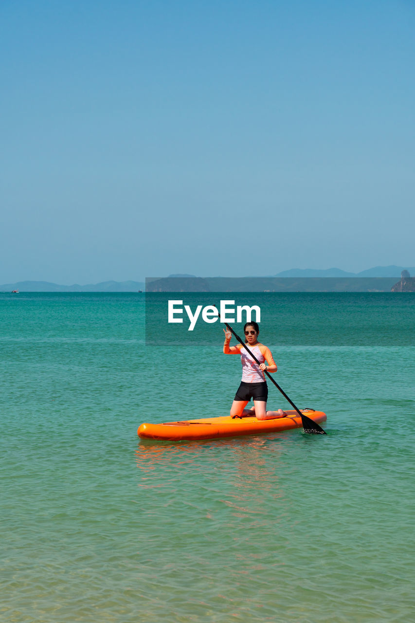 Young sporty woman playing stand-up paddle board on the blue sea in sunny day of summer vacation