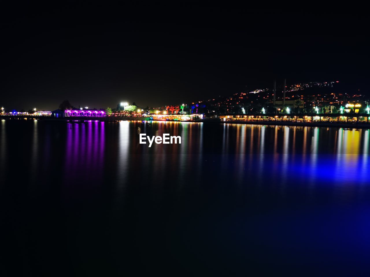 ILLUMINATED BUILDINGS BY RIVER AGAINST SKY