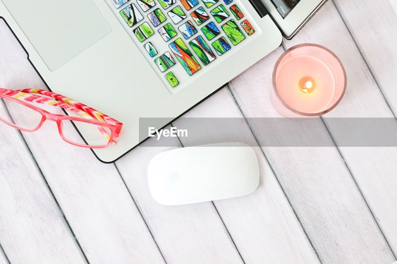 High angle view of laptop with eyeglasses and candle on table