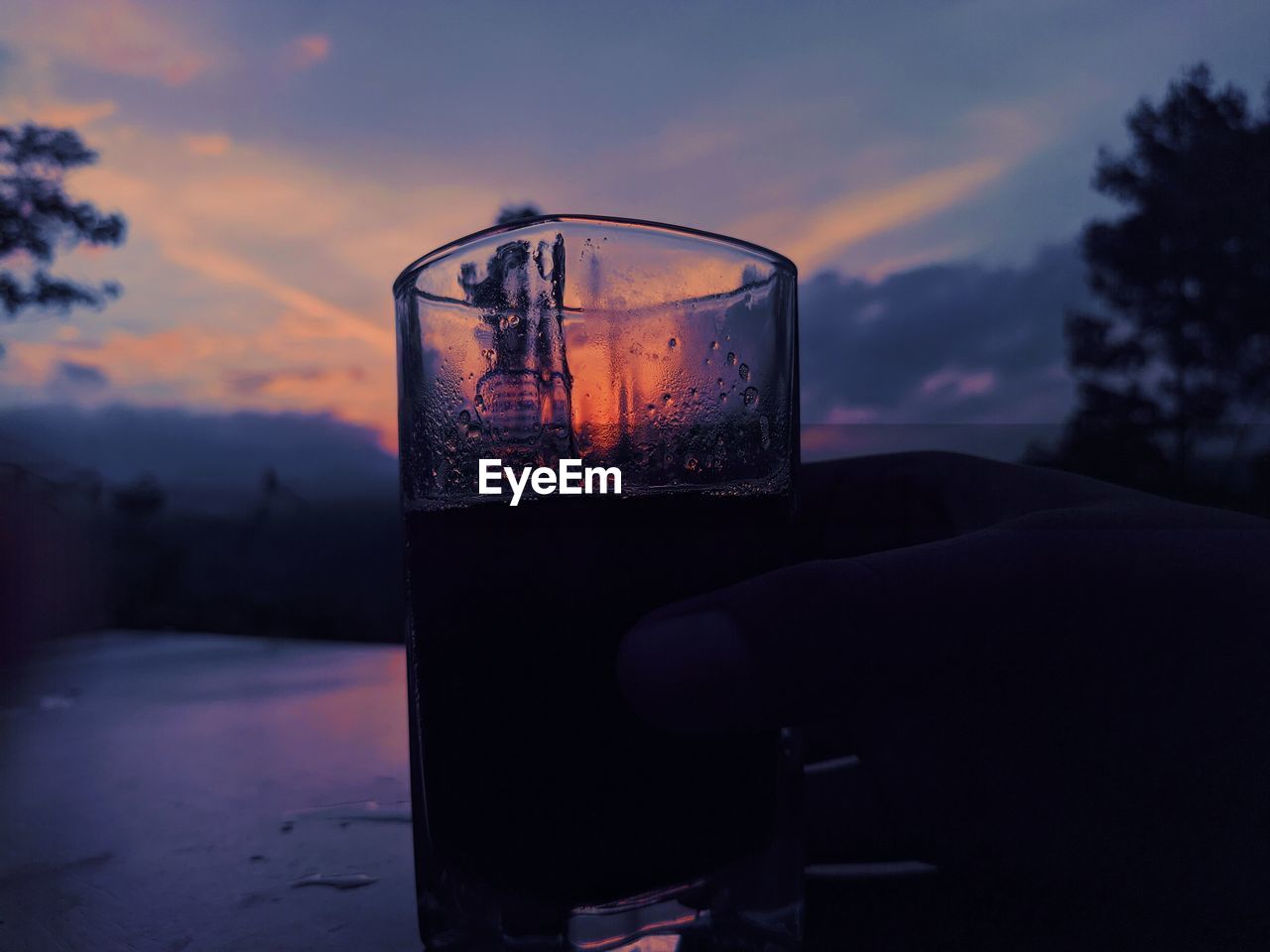 Close-up of beer glass against sunset sky