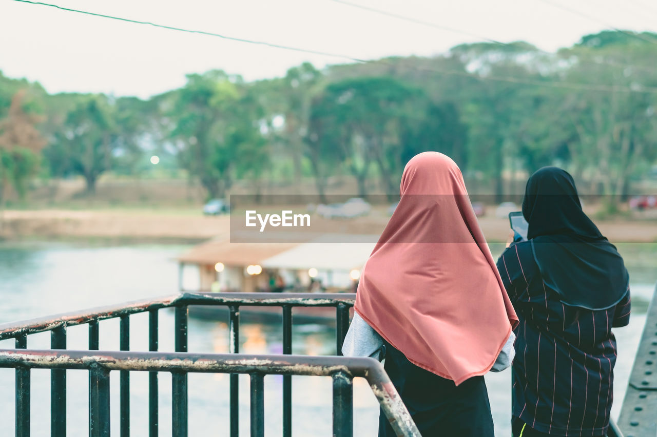 REAR VIEW OF WOMEN STANDING BY RAILING