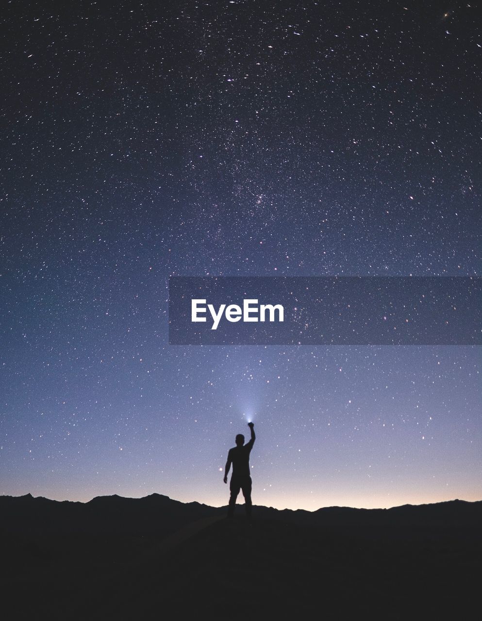 Silhouette man holding flashlight while standing on mountain against star field at night