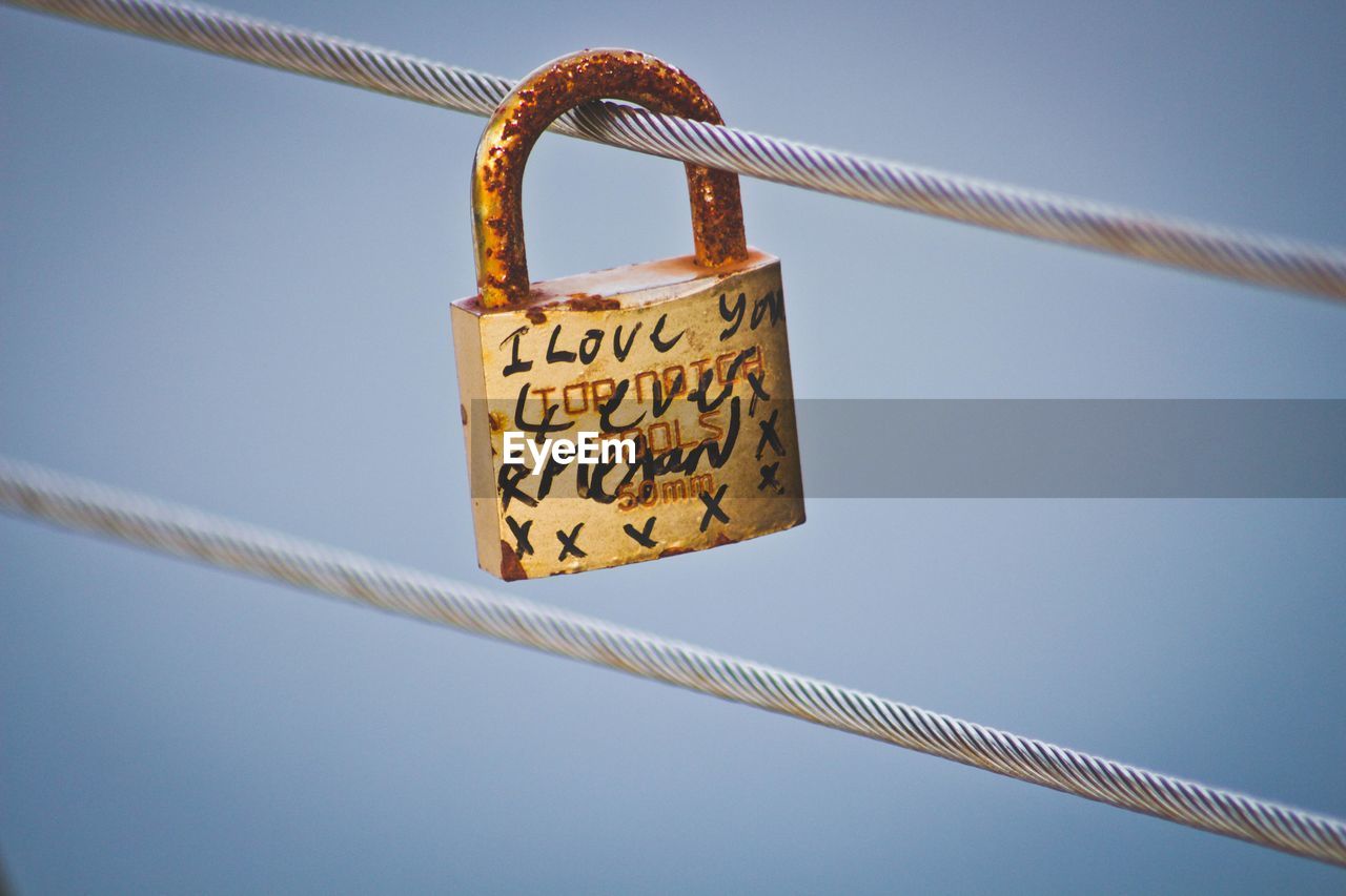 Low angle view of padlocks hanging on cable against sky