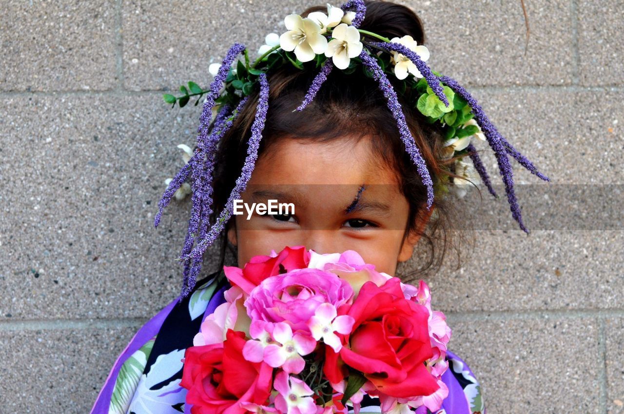 Portrait of cute girl with flowers against wall outdoors