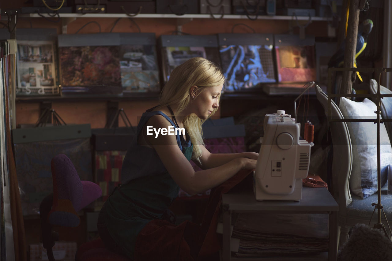 Side view of young fashion designer using sewing machine in studio