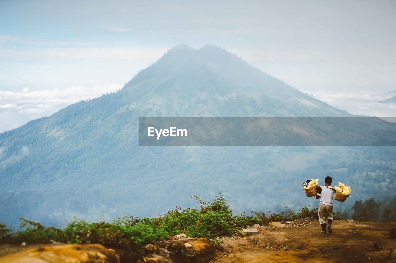 Rear view of man carrying baskets while walking on mountain 