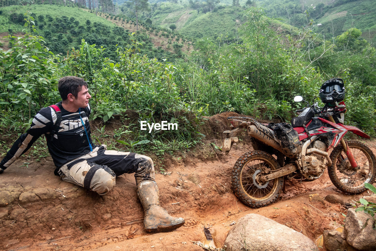 MAN RIDING MOTORCYCLE ON DIRT ROAD IN PARK