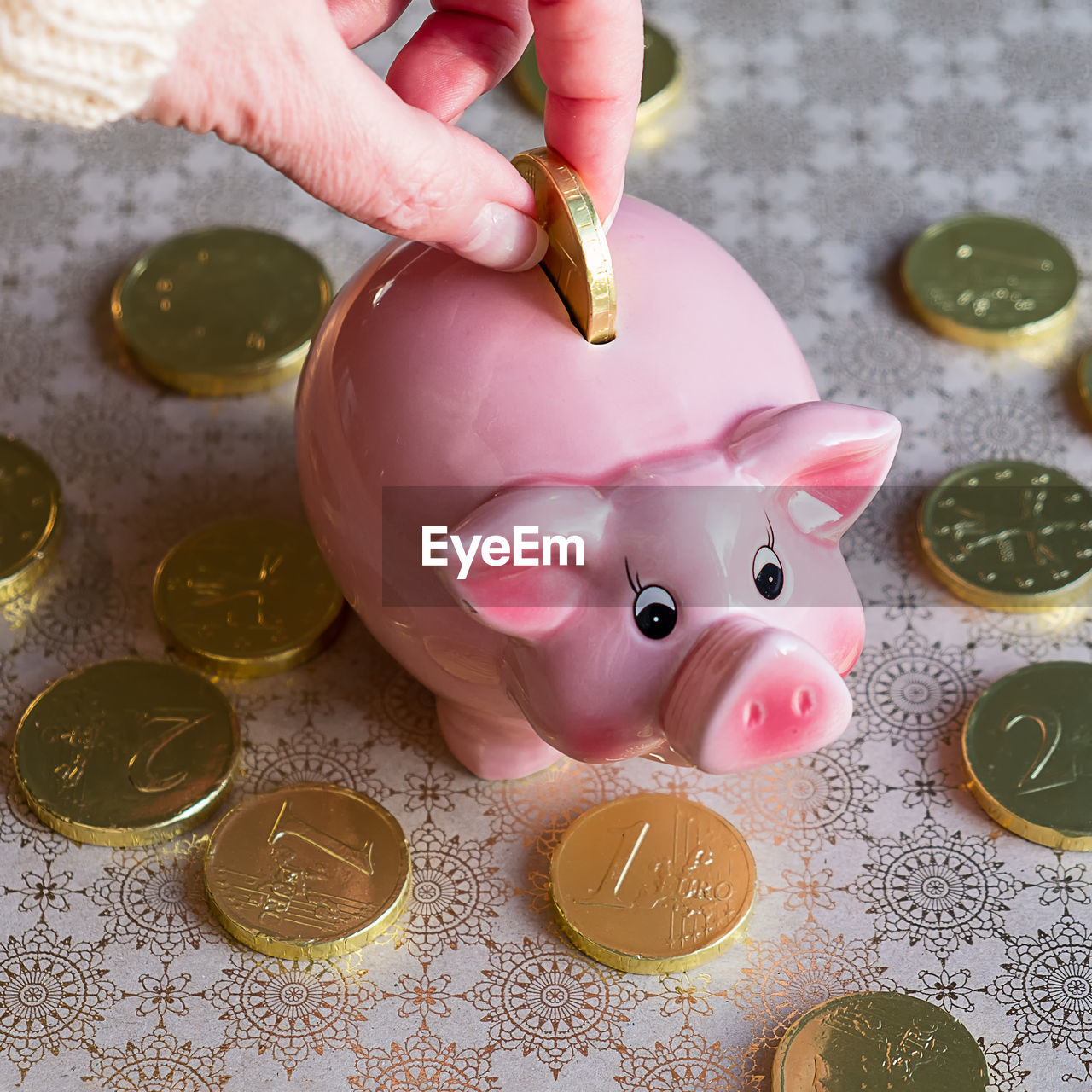 Cropped hand of person inserting coin in piggy bank on table