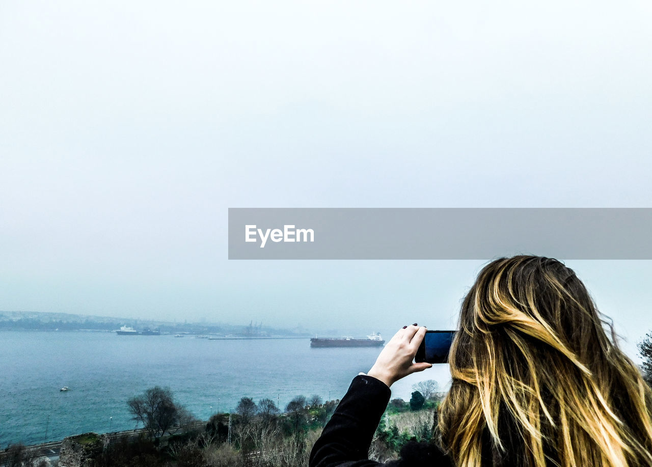 Rear view of woman photographing sea against clear sky