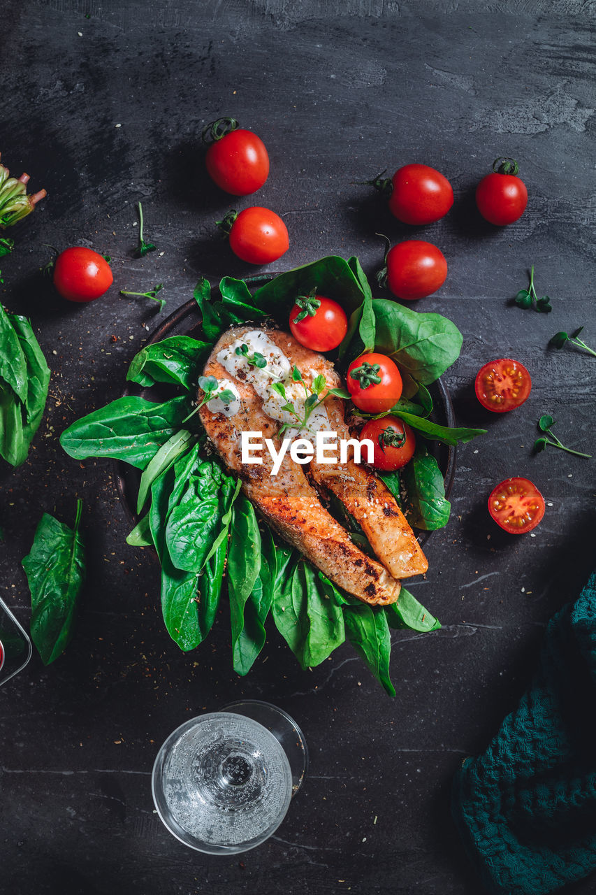 A plate with fresh green raw spinach and fried wild salmon, tomatoes and cream cheese sauce 