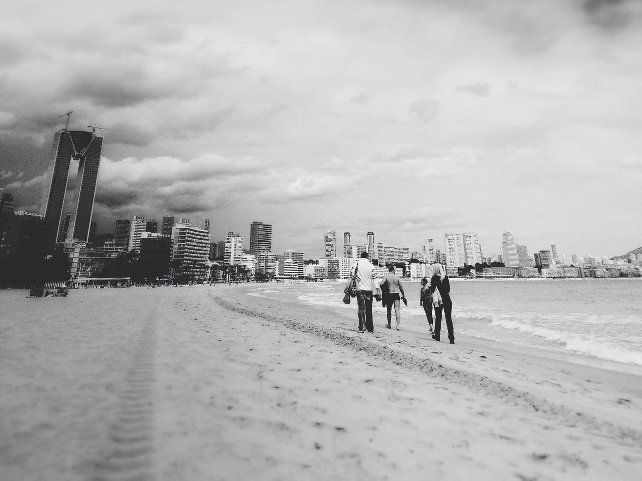 People walking on beach with cityscape in background