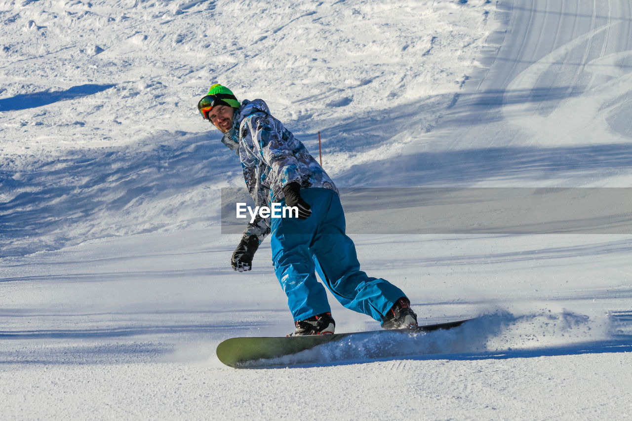 A handsome young man slides down a ski slope on a snowboard. snow flies out from under his board