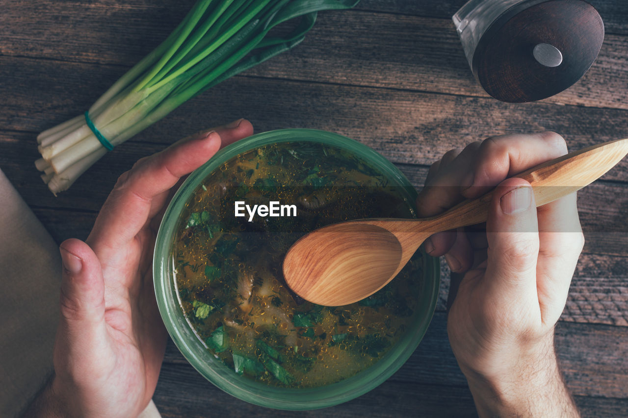 Man eats mushroom soup, green onions, pepper mill and a wooden spoon on old wooden table