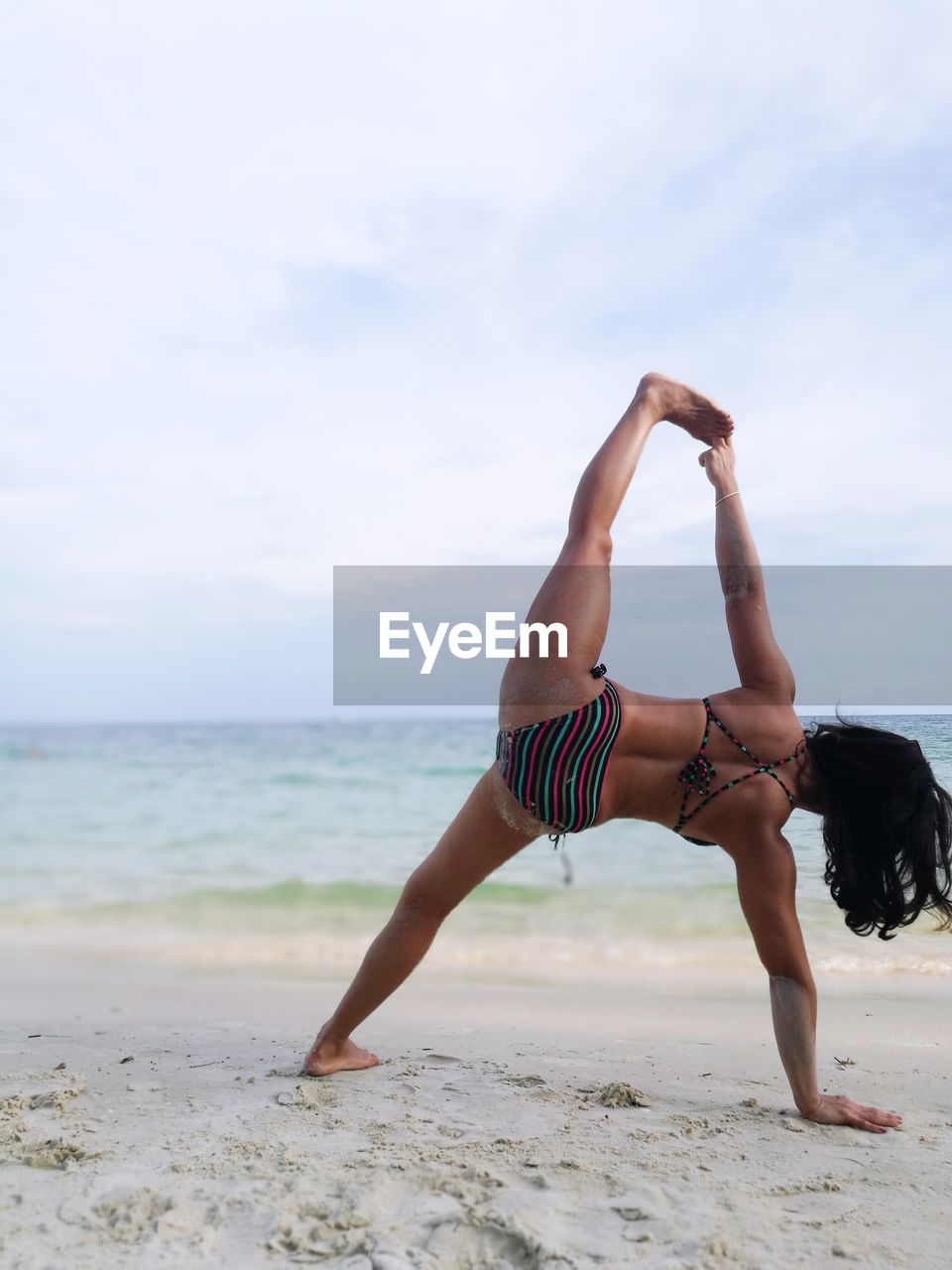 Rear view of woman in bikini stretching at beach