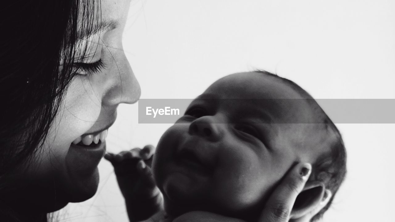 Close-up of smiling mother looking at son against white background