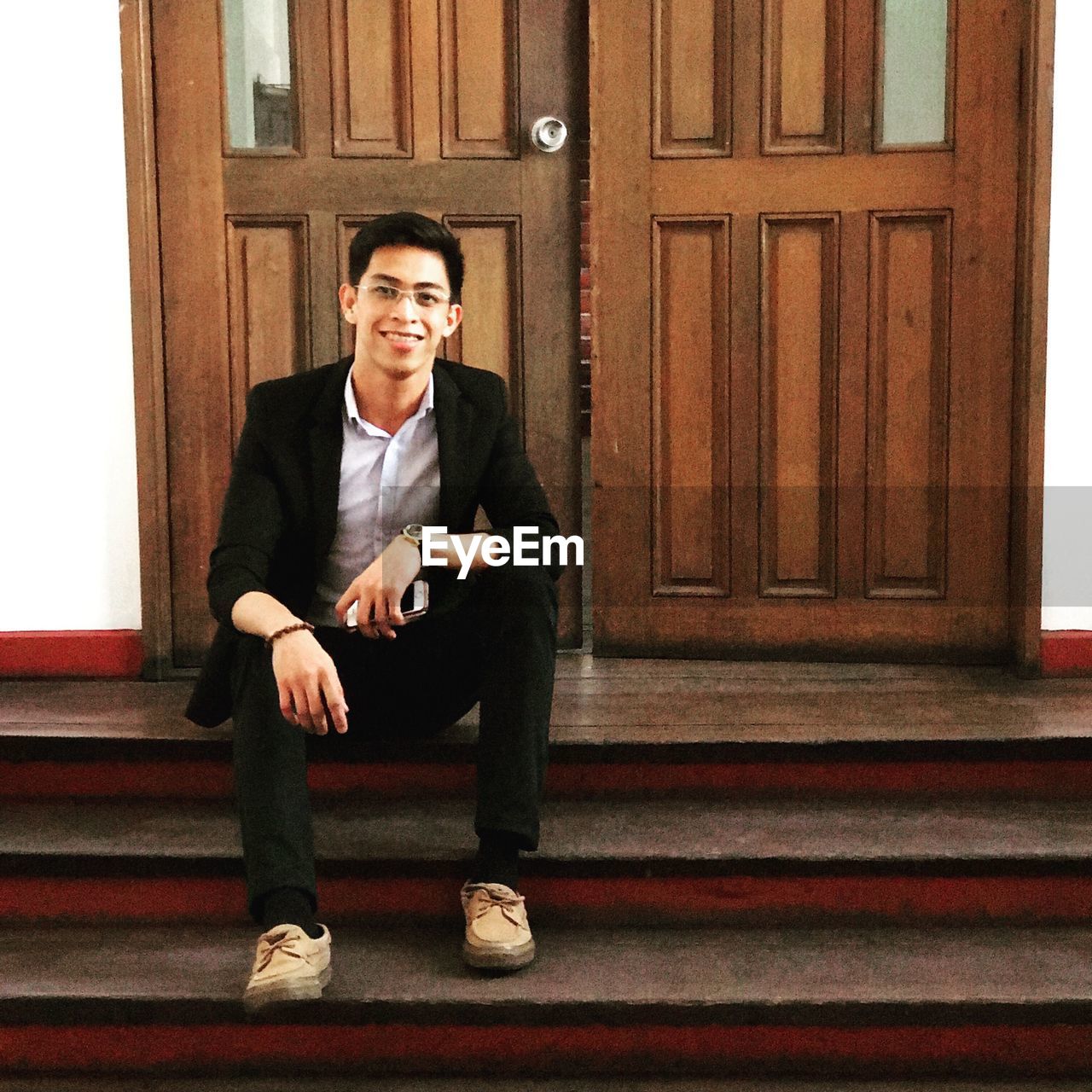 Portrait of young man sitting on steps against door
