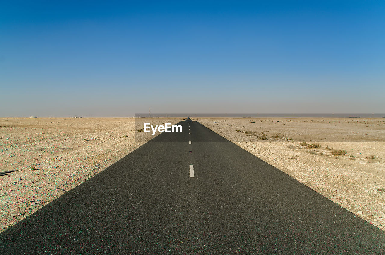 Road leading towards desert against clear sky