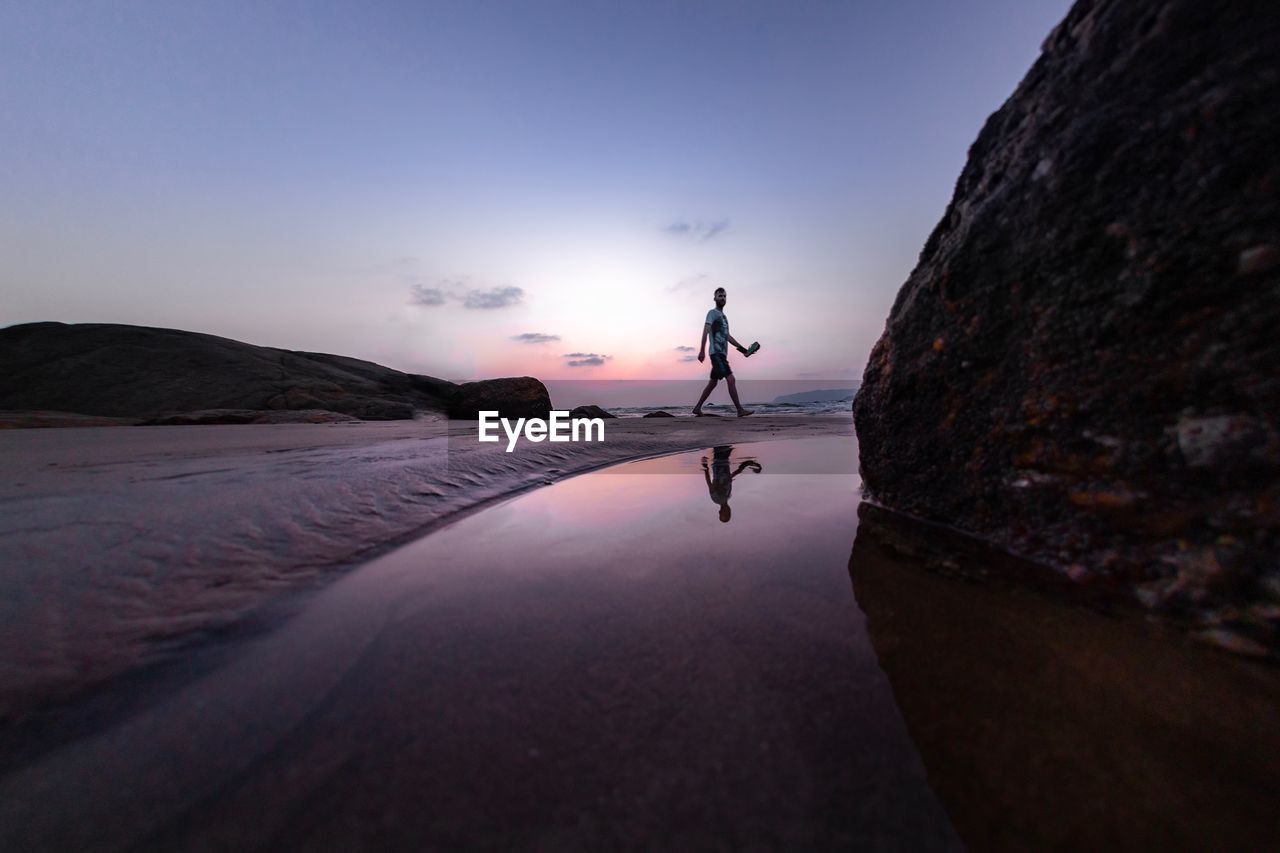 MAN ON ROCK BY SEA AGAINST SKY