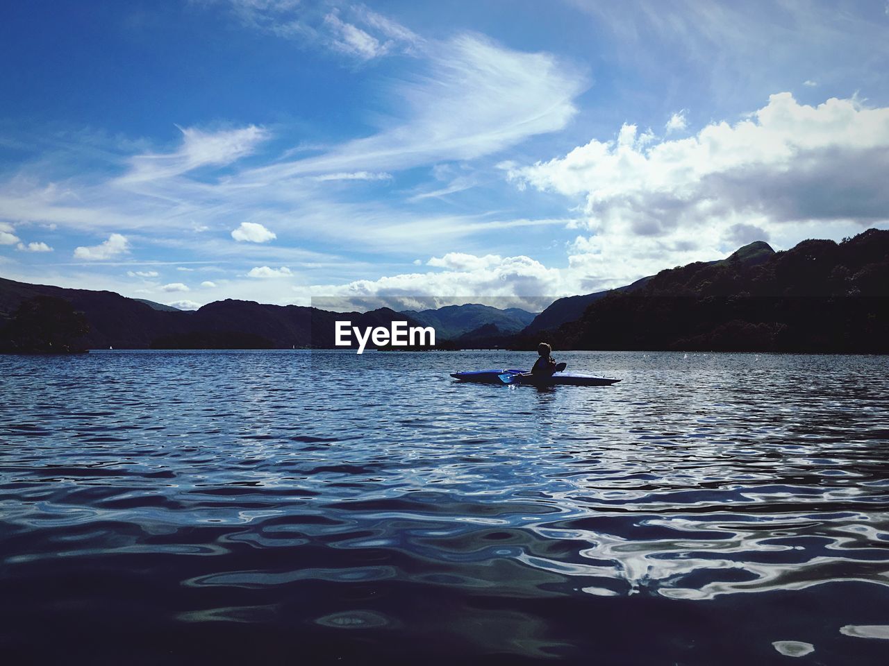 Person kayaking in lake by mountains against sky