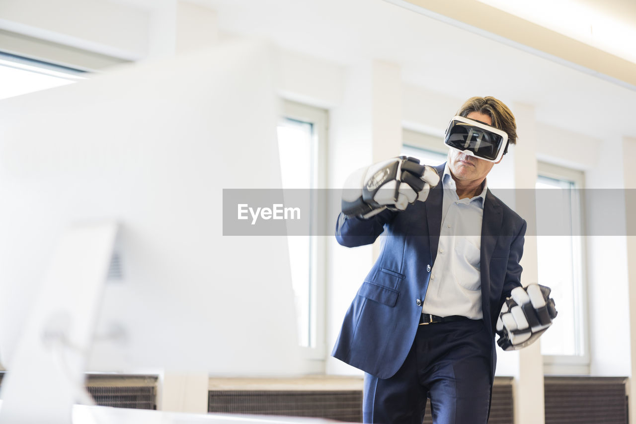 Businessman wearing vr glasses and ice hockey gloves in office