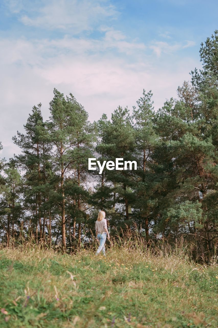 REAR VIEW OF PERSON STANDING ON FIELD AGAINST TREES