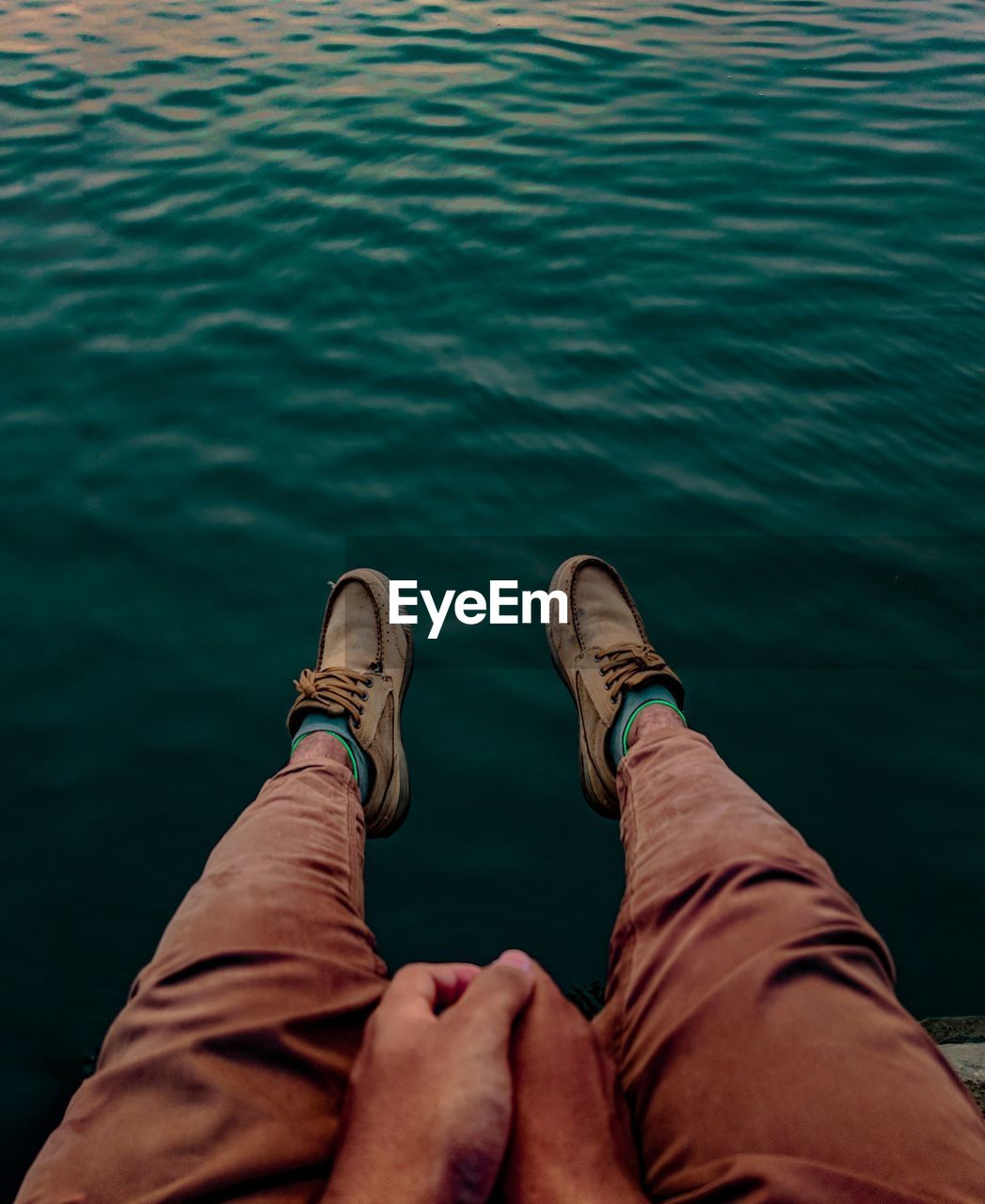 Low section of man sitting on pier over sea