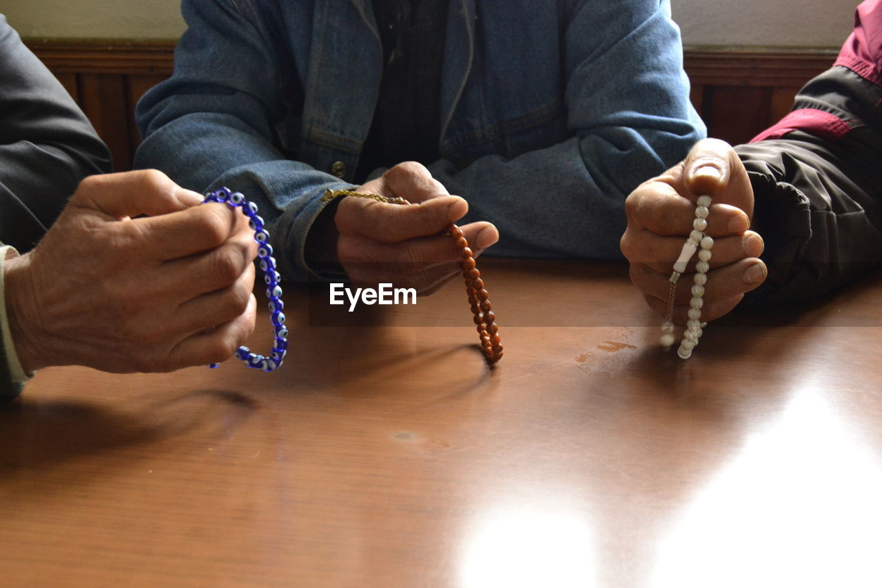 Midsection of people chanting using beads at wooden table