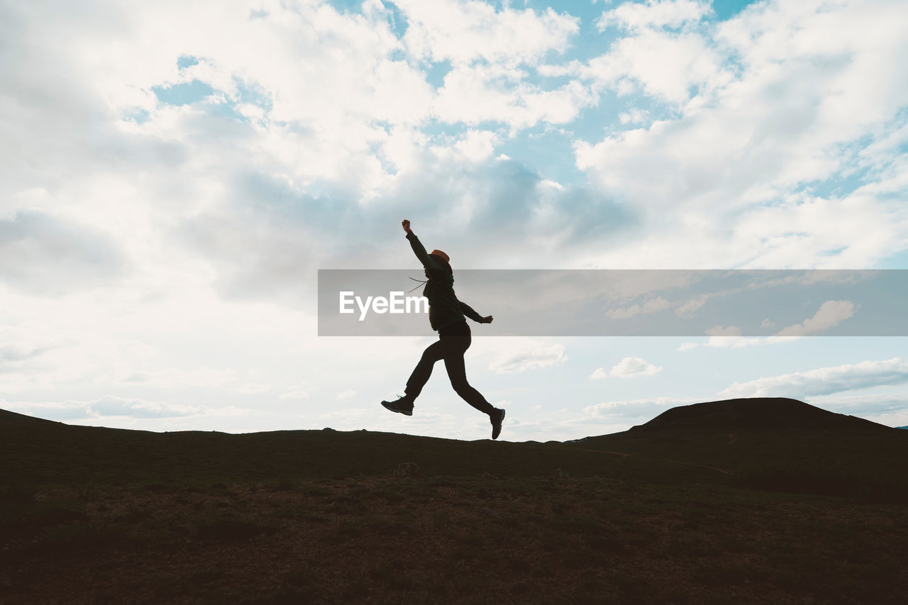 Silhouette mature man jumping on mountain against cloudy sky during sunset