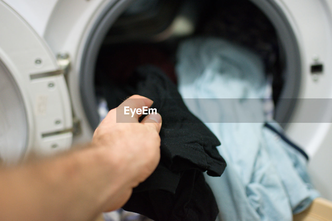 Cropped hand of man washing clothes in machine