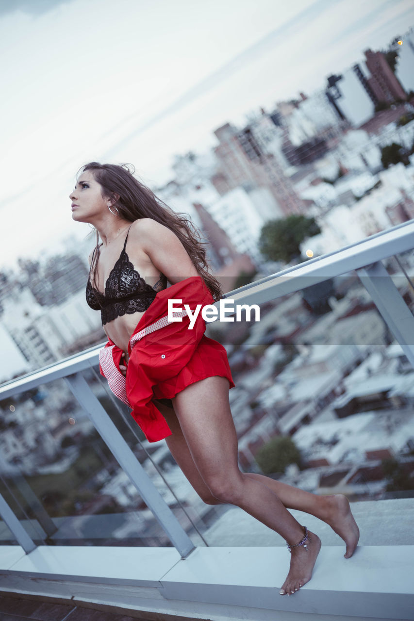 Young woman standing at railing against cityscape