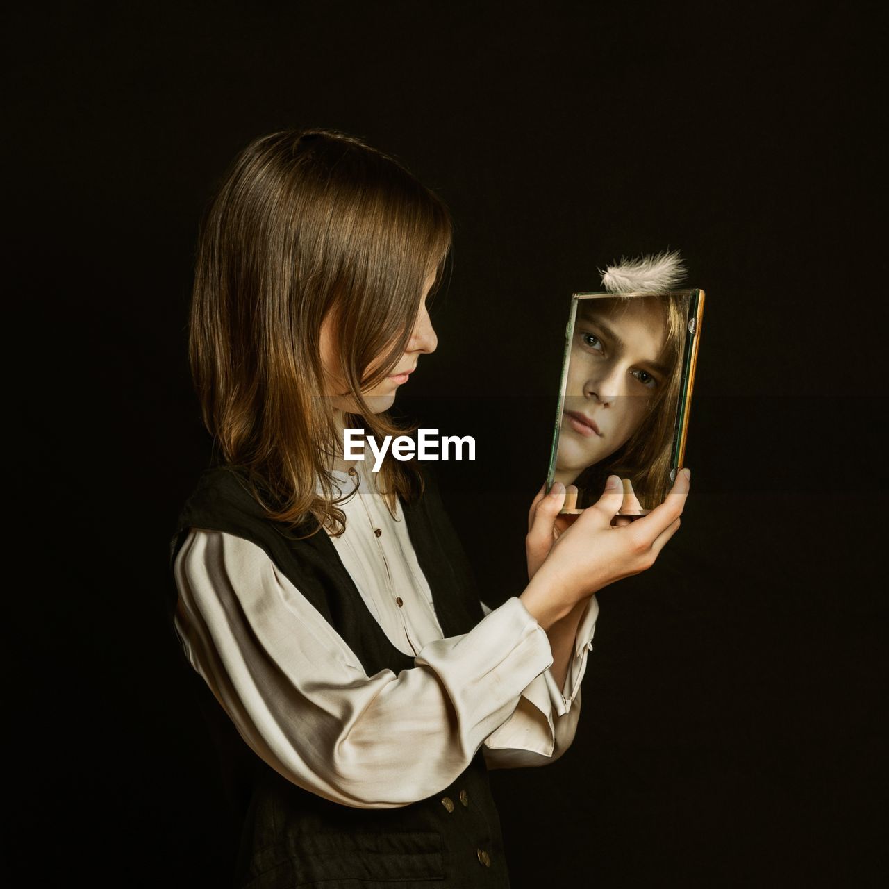 Side view of a kid holding a mirror against black background