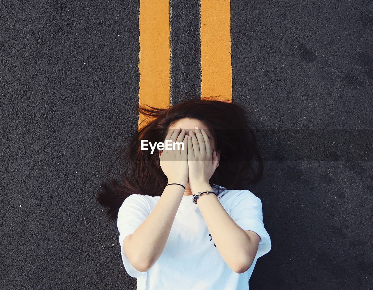 Directly above shot of woman covering face while lying on road