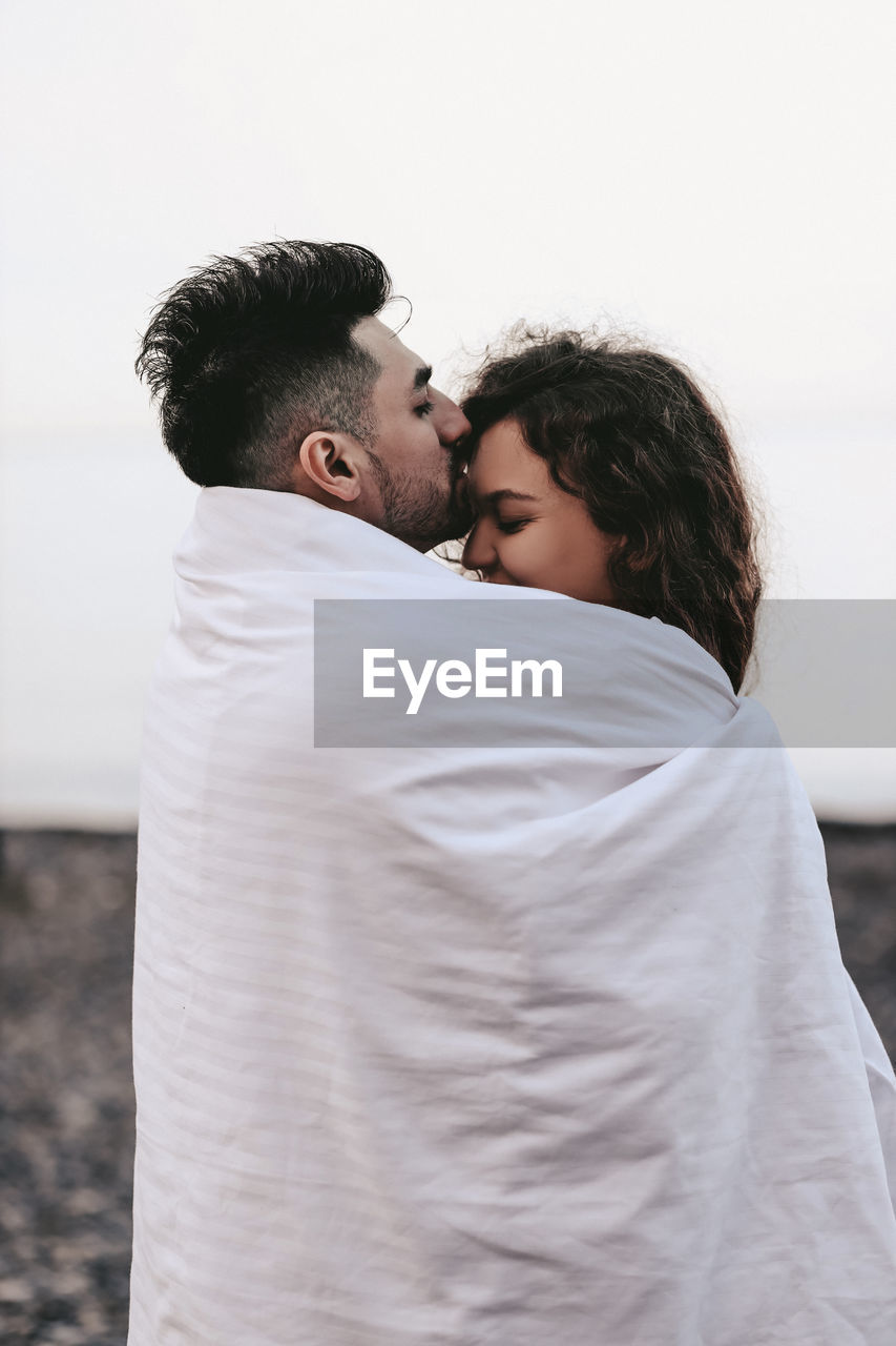 Young couple kissing against clear sky