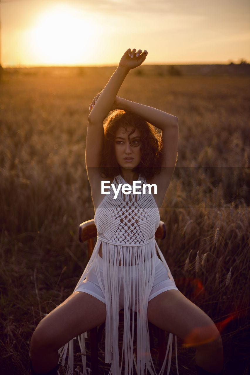 Fashion portrait of a curly-haired woman in white clothes dress sit on a field dry grass in autumn