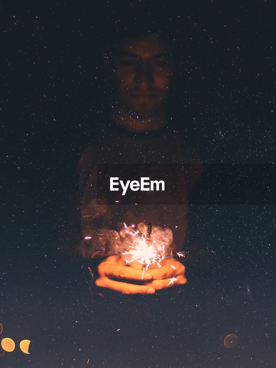 Double exposure of man holding sparkler against star field