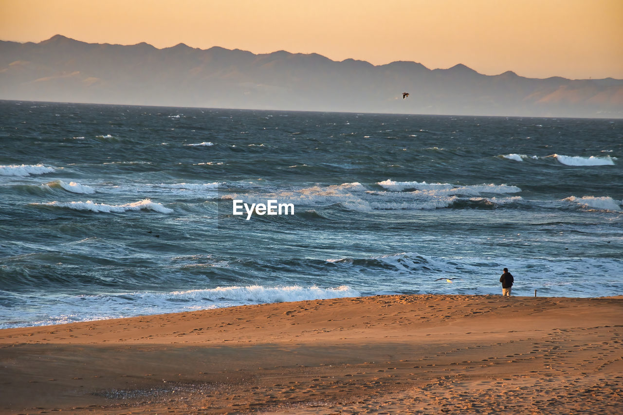 PEOPLE ON BEACH AGAINST SKY DURING SUNSET