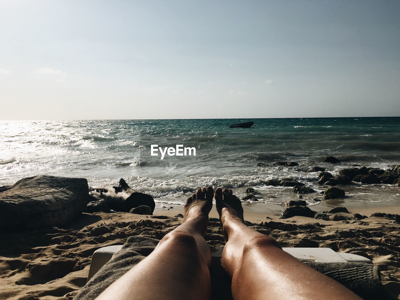 Low section of woman relaxing at beach on sunny day