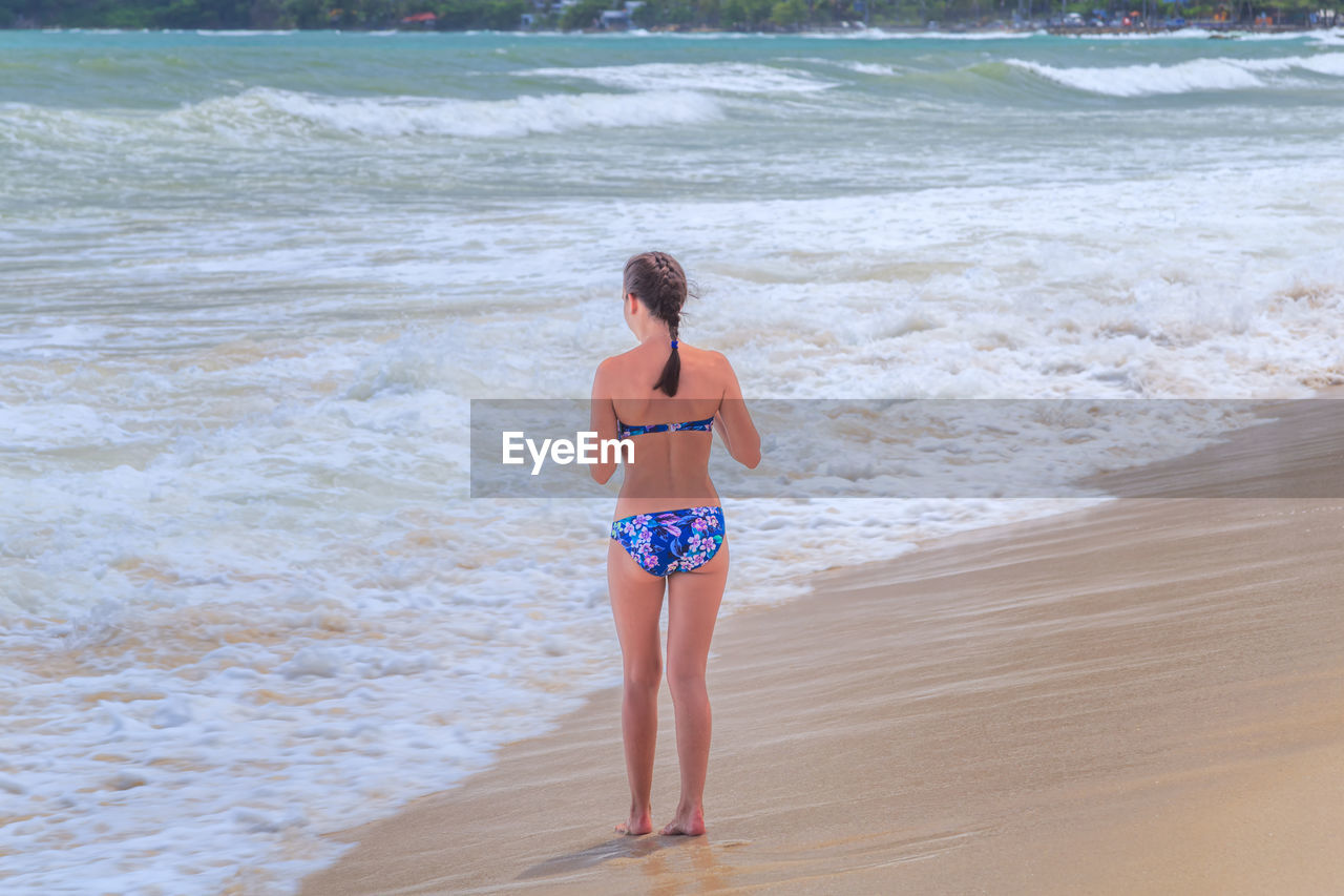 Rear view of woman wearing bikini while standing at beach