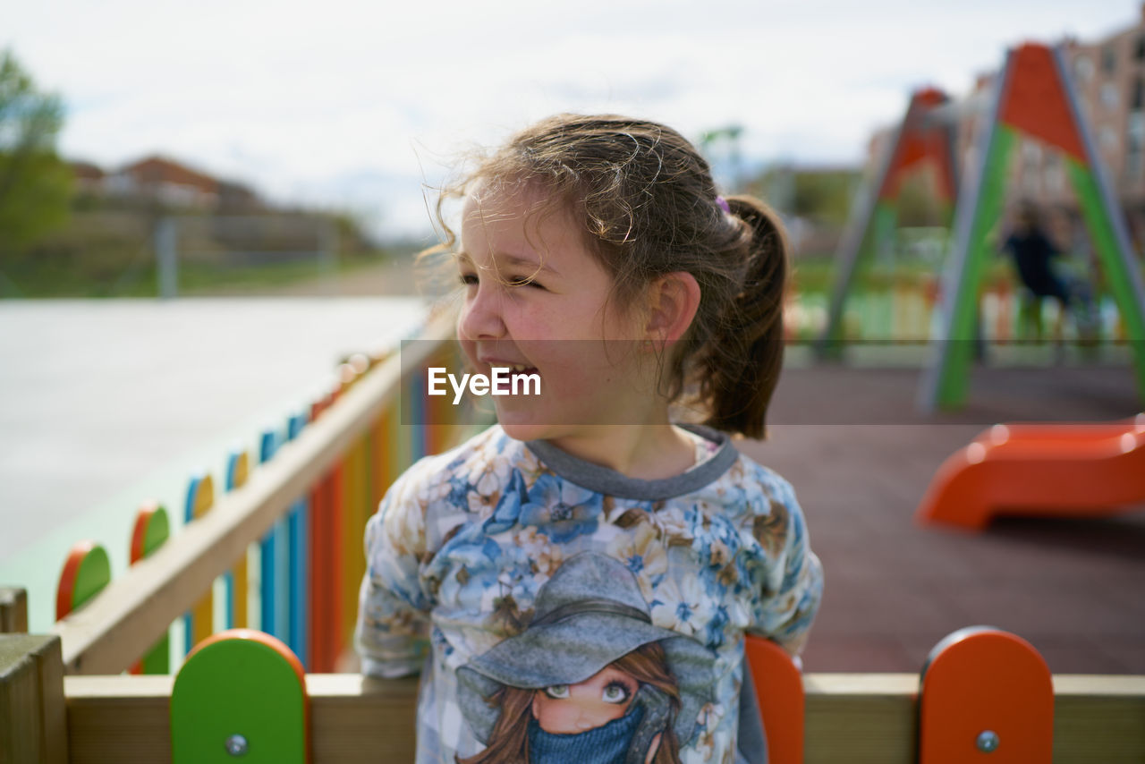 Little girl smiling as she leans on the playground fence