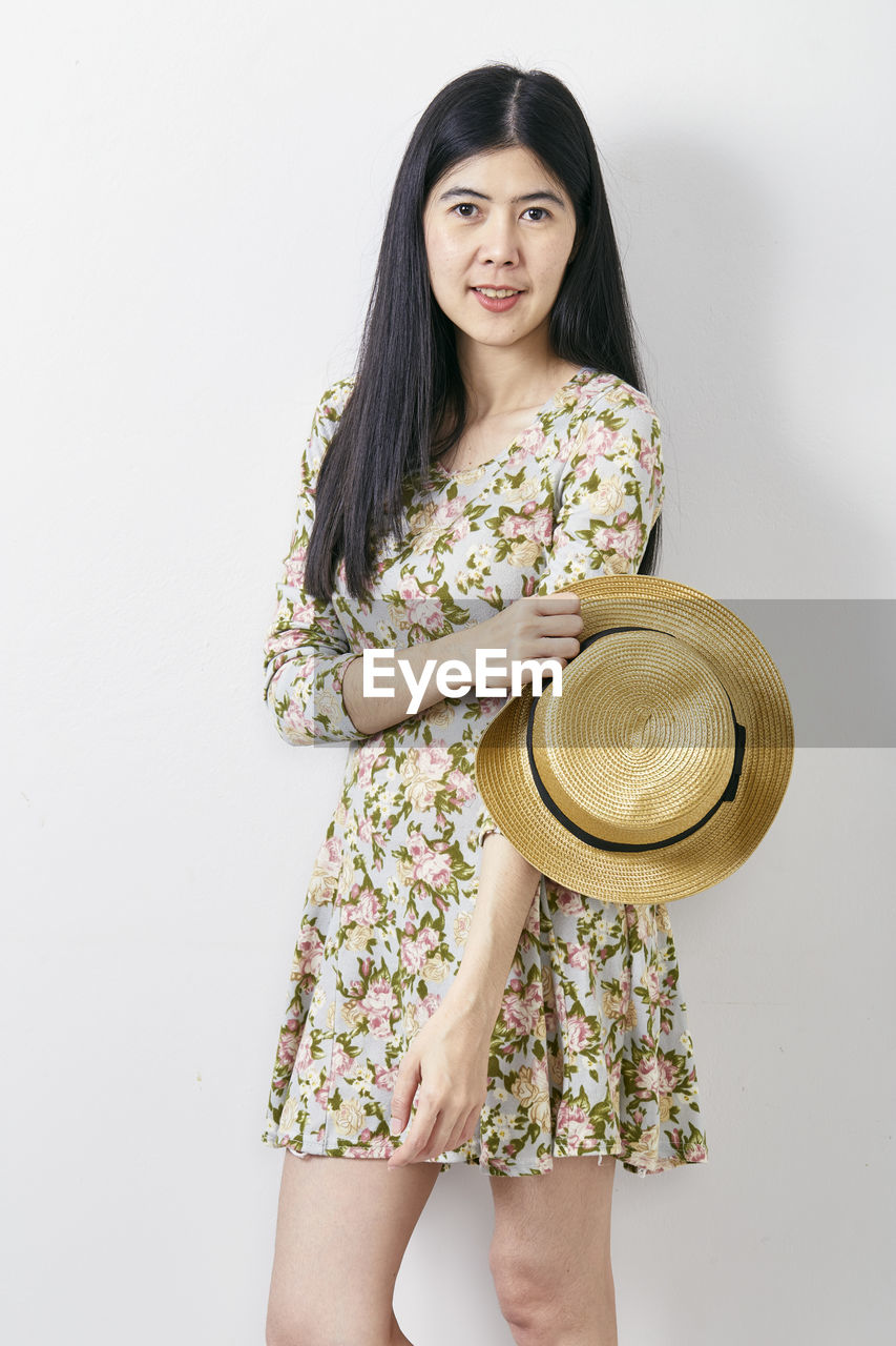 PORTRAIT OF BEAUTIFUL WOMAN WEARING HAT STANDING AGAINST WHITE BACKGROUND