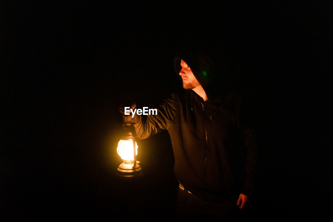 MIDSECTION OF MAN WITH ILLUMINATED LIGHT PAINTING AGAINST BLACK BACKGROUND