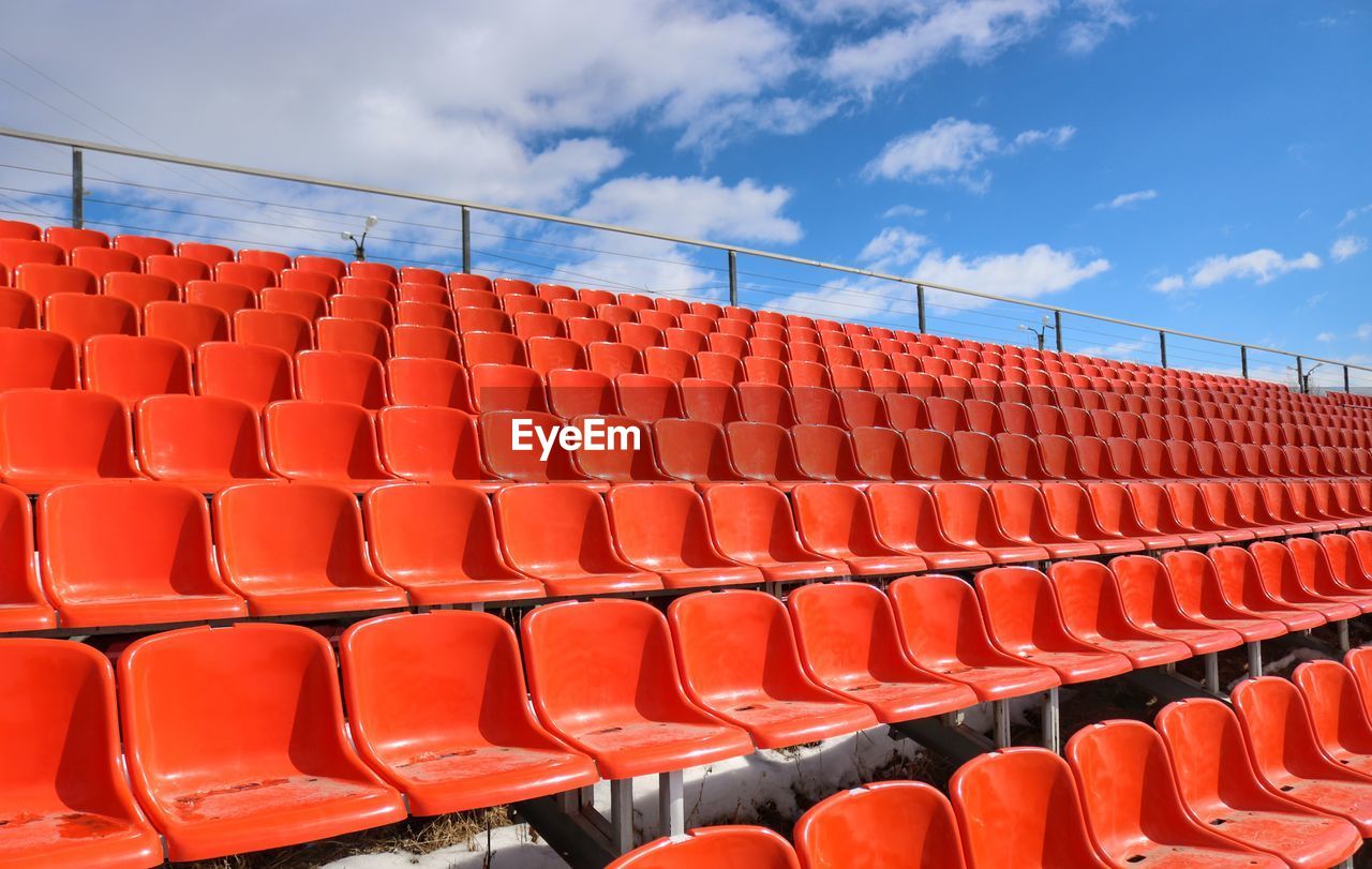 Empty red chairs at stadium against blue sky
