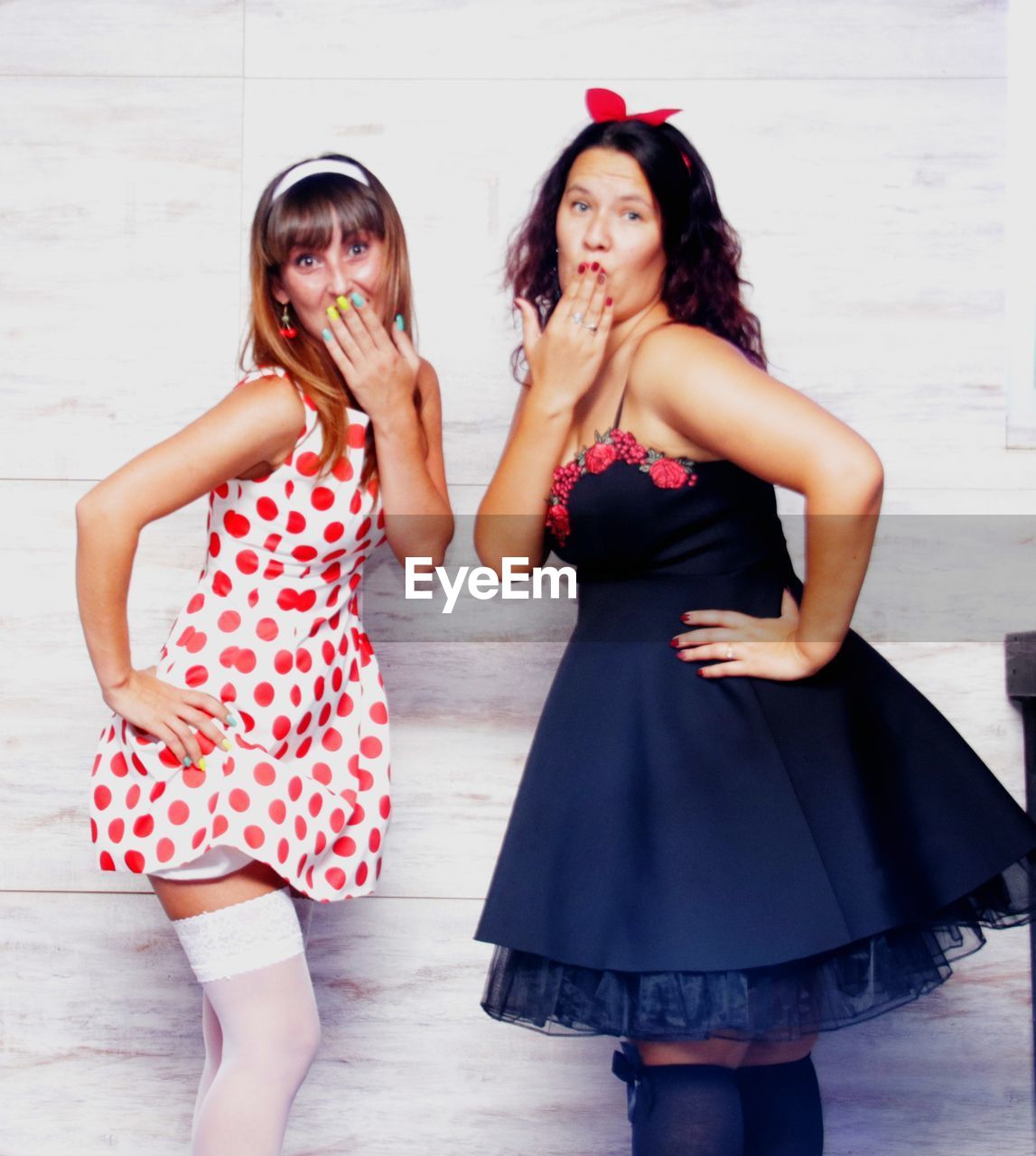 Portrait of female friends covering mouths while standing against wall