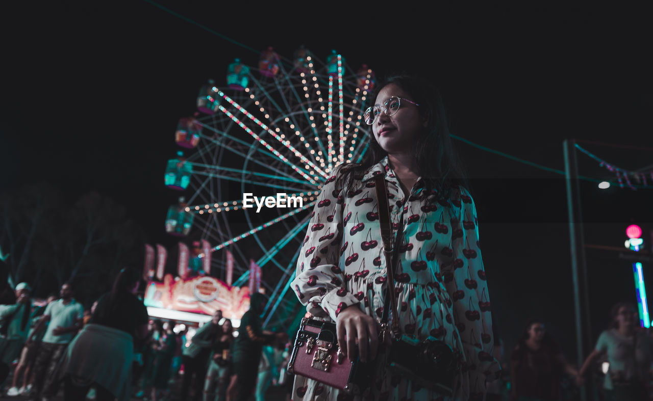 Low angle view of woman standing against ferris wheel at night