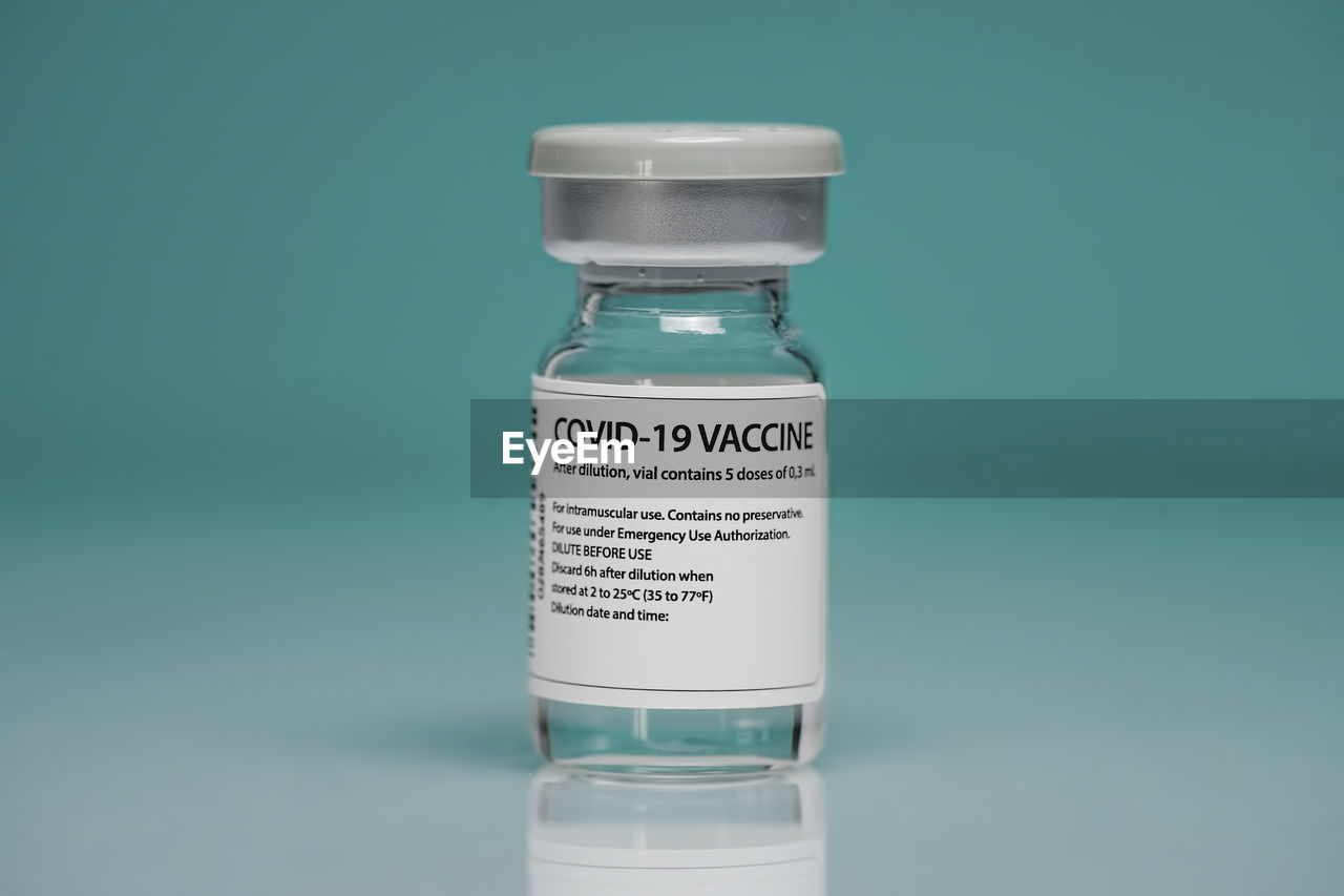 Medical glass vial with coronavirus vaccine placed against blue background