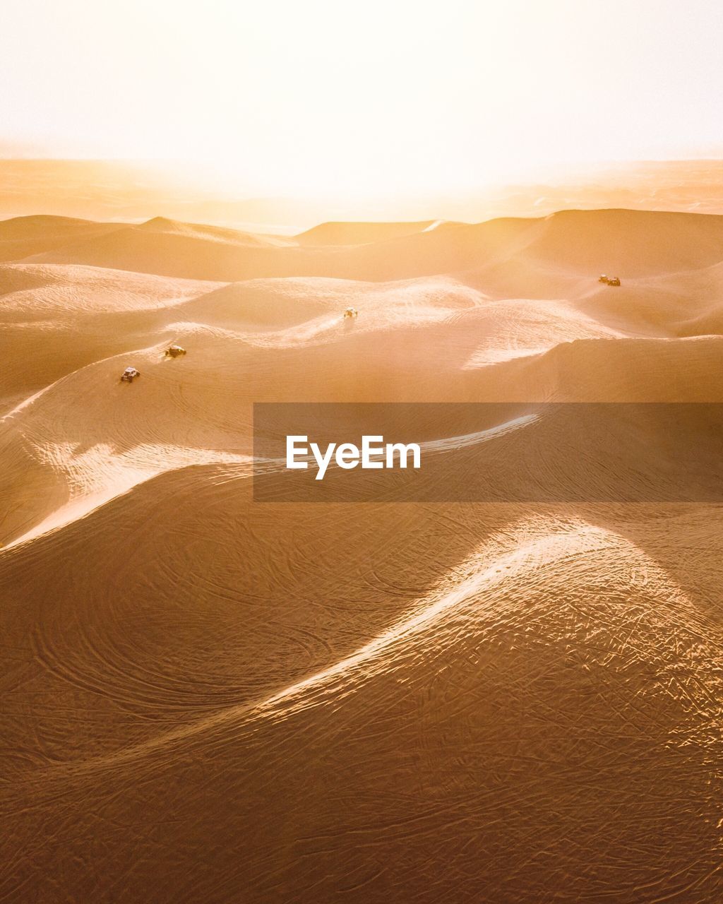 Bright sunlight shining over the dunes in glamis california as dune buggies race across the sand