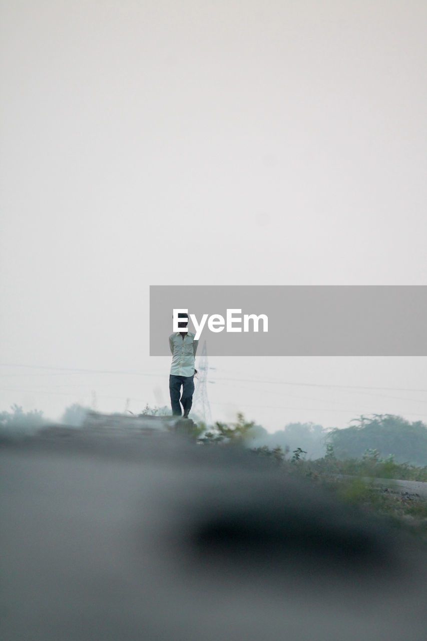 MAN WITH UMBRELLA STANDING ON ROAD AGAINST SKY