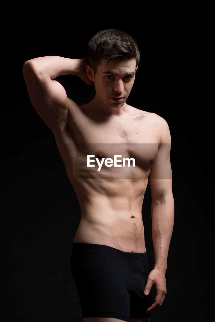 Portrait of shirtless male model standing against black background