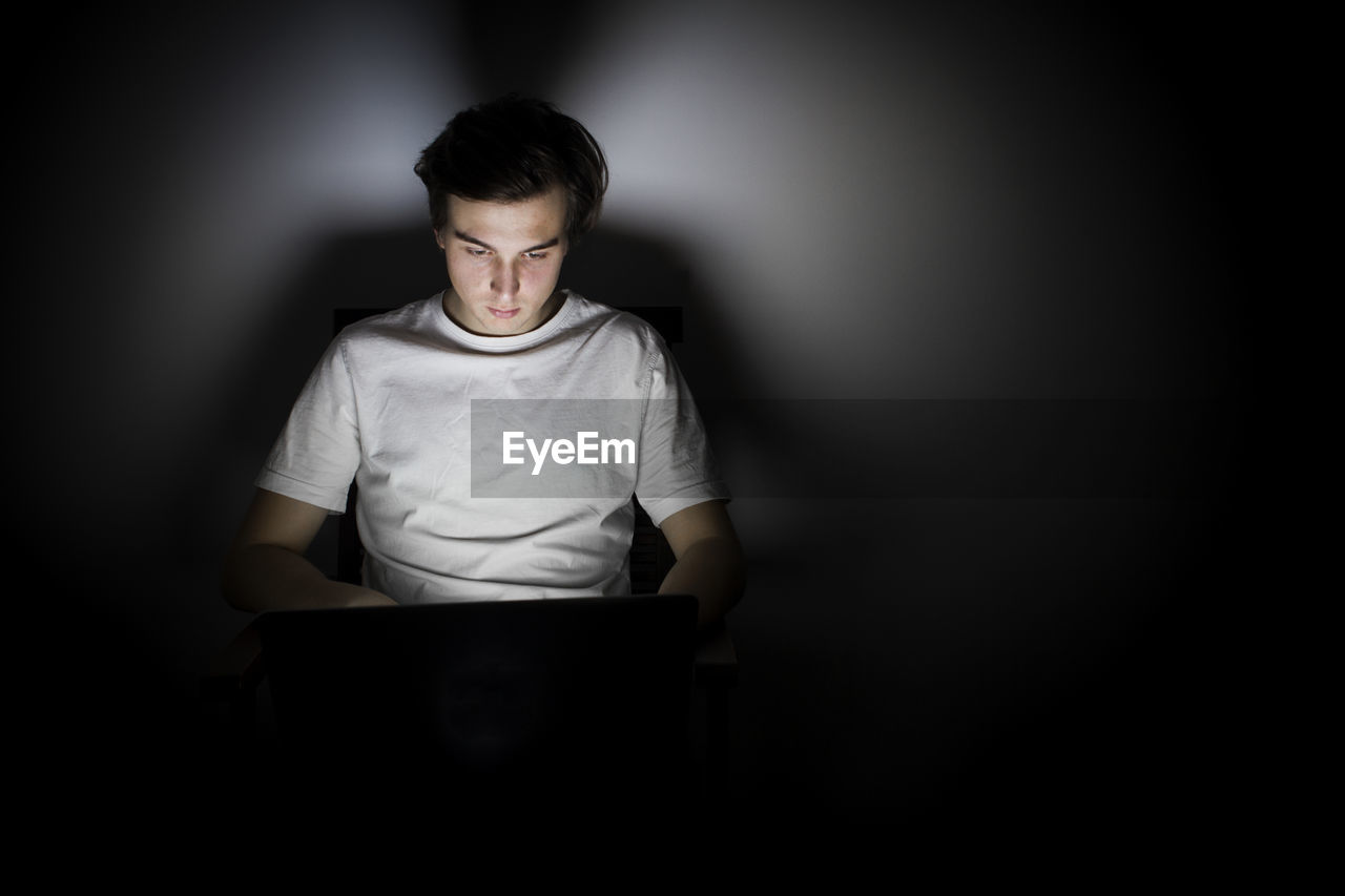 Young man using laptop in darkroom